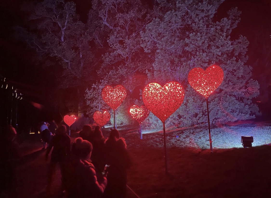 Glowing red heart light sculptures on posts along a grassy slope at Kingston Lacy at night